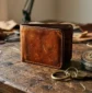 Weathered full-grain leather wallet with rich patina, vintage brass key ring, and natural leather balm tin on a rustic oak workbench – Roaming Lifestyle