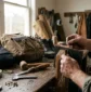 Craftsman's hands stitching vegetable-tanned leather using a wooden pony on a cluttered workbench in a sunlit artisan workshop – Roaming Lifestyle