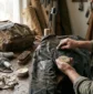 Hands applying natural canvas wax bar to a rugged field jacket on an oak workshop bench next to a hairdryer, brush, and waxed rucksack – Roaming Lifestyle