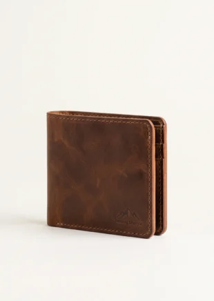 Handcrafted closed tobacco brown full-grain leather bifold wallet with contrast stitching and debossed mountain crest logo on a plain studio background – Roaming Lifestyle