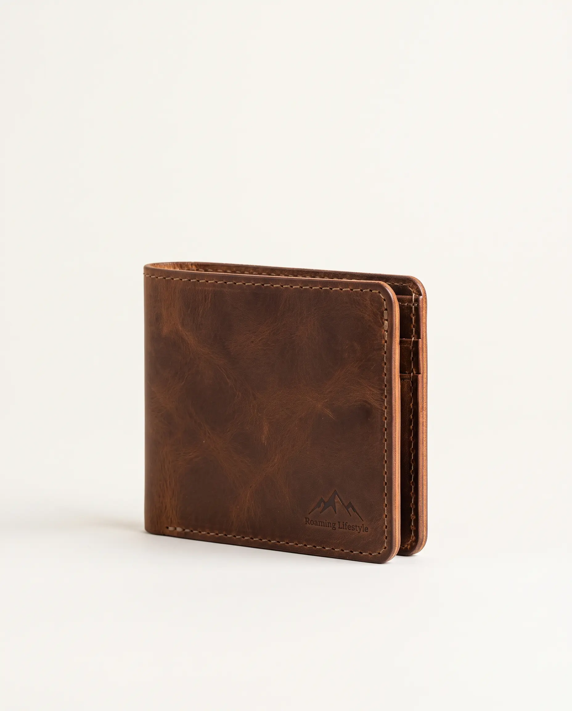 Handcrafted closed tobacco brown full-grain leather bifold wallet with contrast stitching and debossed mountain crest logo on a plain studio background – Roaming Lifestyle
