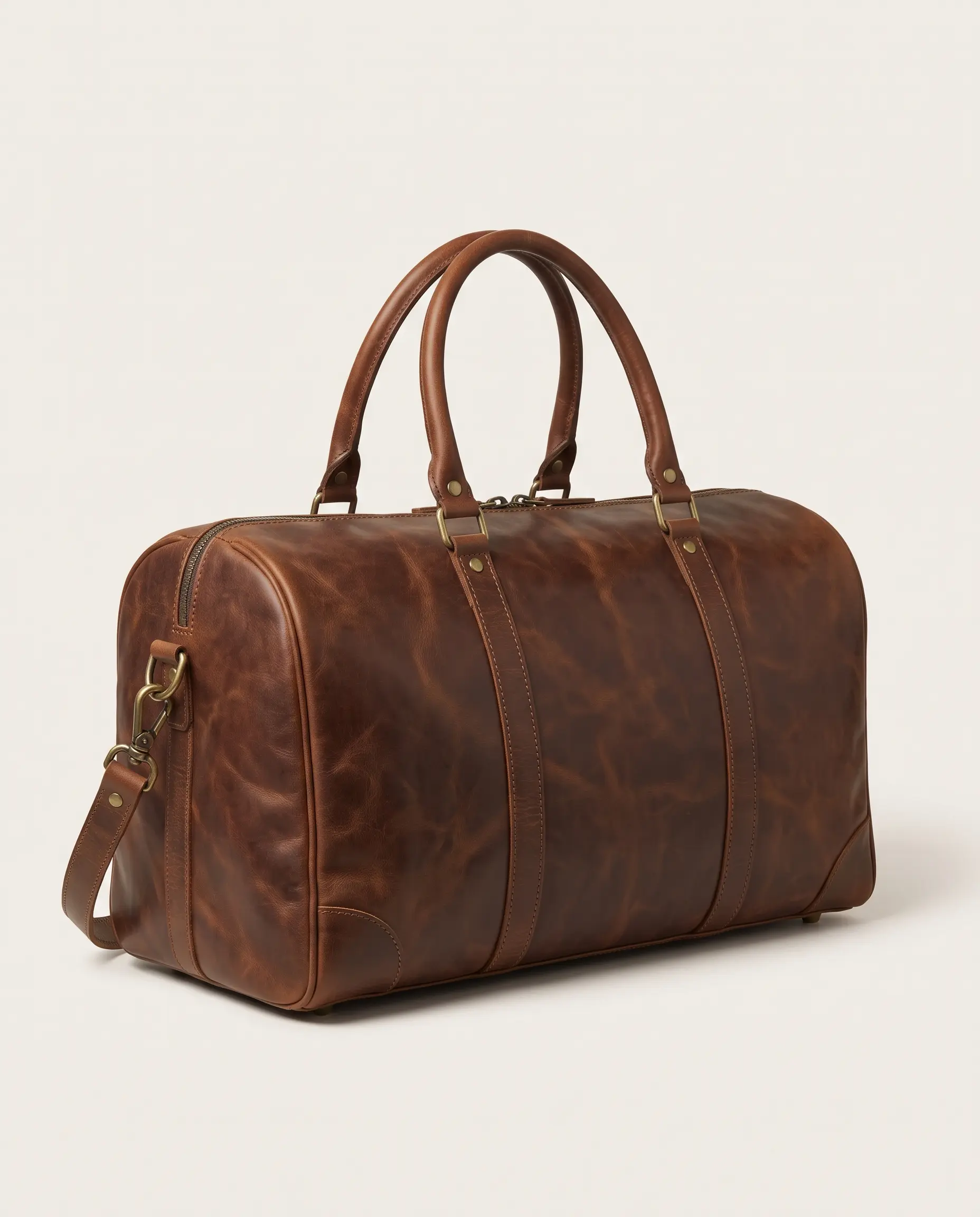 Back and side view of brown full-grain leather weekender duffle bag with top handles, d-rings, base reinforcement, and protective brass feet on a studio background – Roaming Lifestyle