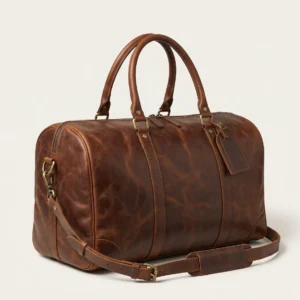 Handcrafted brown full-grain leather weekender duffle bag with top handles, brass hardware, luggage tag, and detachable shoulder strap on a studio background – Roaming Lifestyle