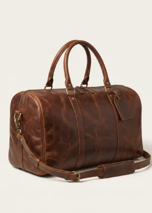 Handcrafted brown full-grain leather weekender duffle bag with top handles, brass hardware, luggage tag, and detachable shoulder strap on a studio background – Roaming Lifestyle