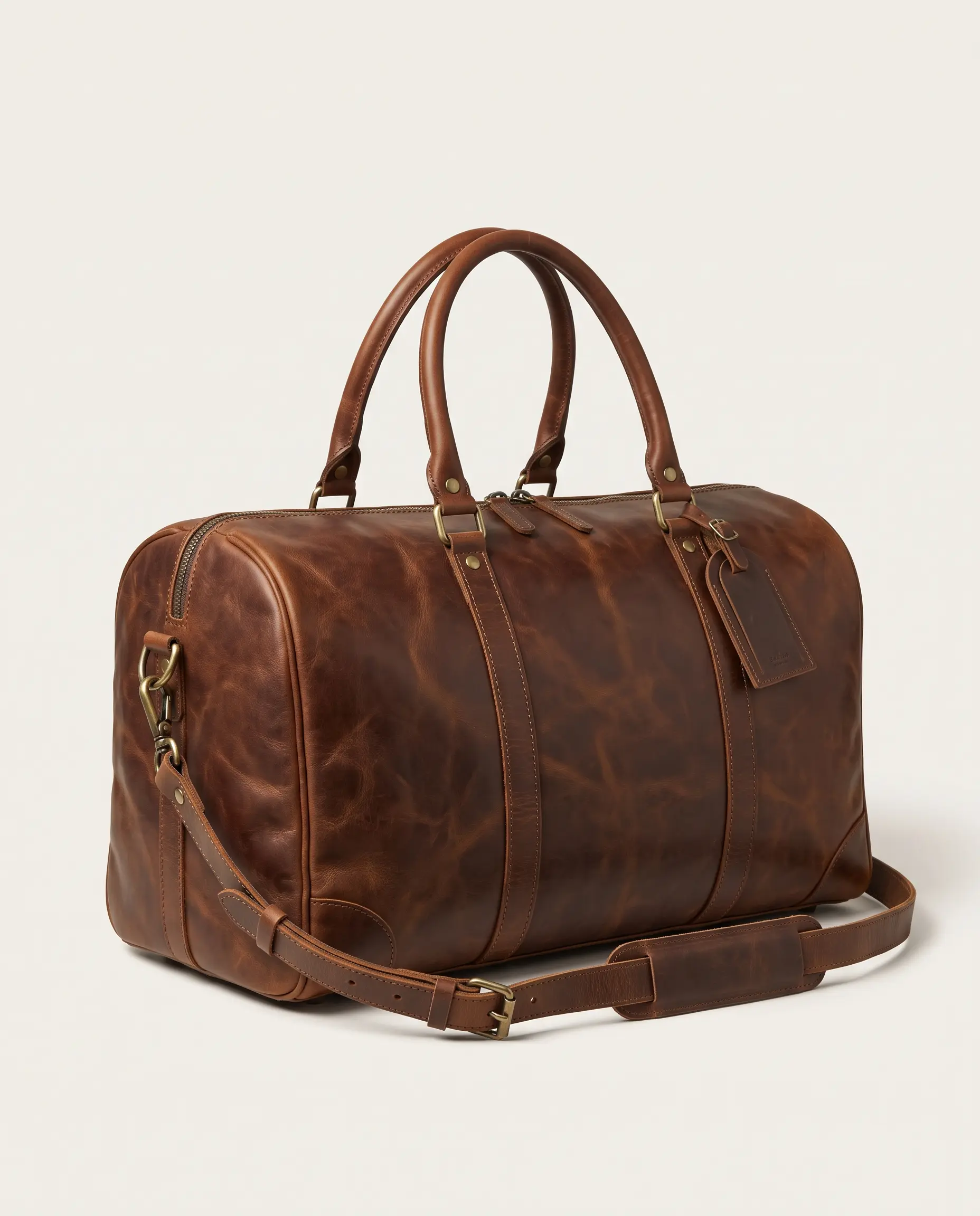 Handcrafted brown full-grain leather weekender duffle bag with top handles, brass hardware, luggage tag, and detachable shoulder strap on a studio background – Roaming Lifestyle