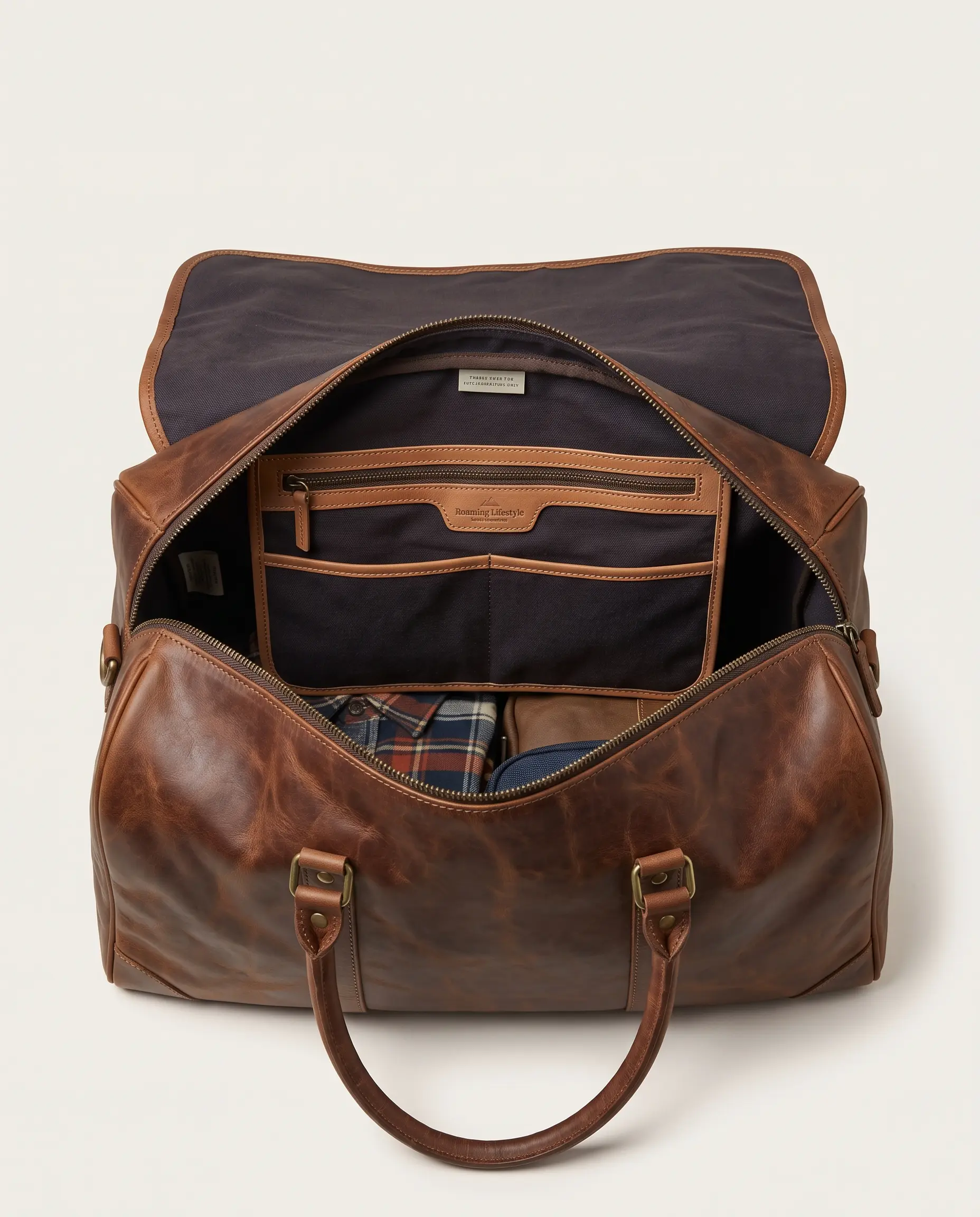 Open top view of brown leather weekender duffle bag showing dark canvas lining, organizer zip pocket, slip pouches, and packed travel clothes on plain studio background – Roaming Lifestyle